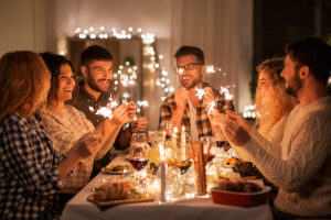 Celebration and people concept - happy friends with sparklers having Christmas dinner at home